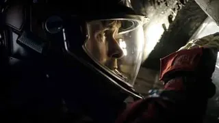 In a dark, narrow space, astronaut Ryland Grace (Ryan Gosling), in a full spacesuit and helmet, peers through a small opening in Project Hail Mary