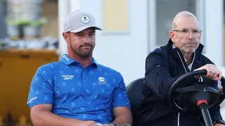 Bryson DeChambeau is driven on a buggy by an Open rules official