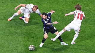Lionel Messi of Argentina in action with Harry Kane and Anthony Gordon of England during Argentina's World Cup semi-final win against England. Kane is on the ground and Gordon's left leg looks to be swinging towards Messi as the England players, in white, try to dispossess Argentina's captain, in dark blue.