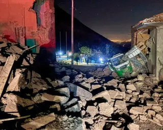 A motor tricycle pokes out amid the rubble caused by the earthquake; in the background, rescuers can be seen, holding torches