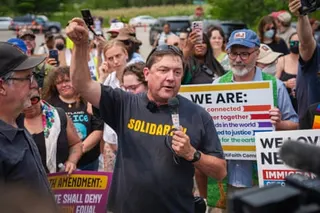 a man speaks into a microphone in front of a crowd of people outside