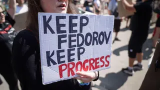 A young woman holds a sign which says 'KEEP FEDOROV, KEEP PROGRESS'