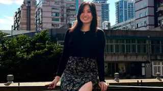 年輕投資者米歇爾·黃坐在欄杆上，在藍天和住宅區前擺姿勢拍照。