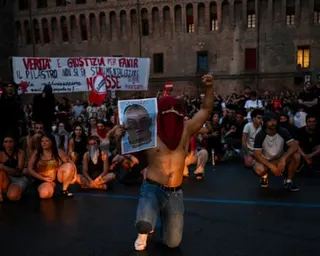 A shirtless protester kneels, raises a fist and holds a portrait of Abderrahim Fakir as dozens more sit and crouch on the ground behind him