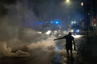 Protester silhouetted against clouds of teargas on street at night