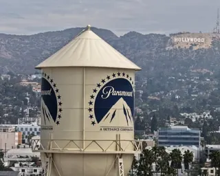 A water tower with the Paramount logo stands against hills with the Hollywood sign visible in the distance