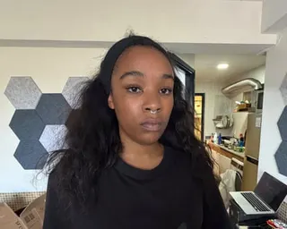 Isabel Rose: she is black, with long, wavy hair worn loose, and has a septum ring in her nose. She wears a black top and is photographed in what appears to be a modern apartment with a kitchen area in the background.