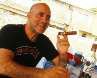 Daniel Siad in black T-shirt holds a lit cigar and smiles at the camera