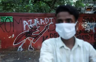 A supporter of India’s Cockroach Janata party (CJP) stands next to a graffiti of a cockroach holding a pen at the ongoing protest site at Jantar Mantar in Delhi.