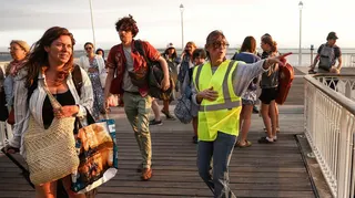 A volunteer gives indication to holidaymakers from Lege-Cap-Ferret upon their arrival in Arcachon by boat during an evacuation operation of the entire Cap-Ferret peninsula, in southwestern France, on July 24, 2026 whilst a wildfire is spreading across the area