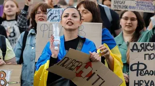 Ukrainians, including a young woman draped in a Ukrainian blue-and-yellow flag, hold placards reading 'Bring him back" during a protest against the dismissal of Defence Minister Mykhailo Fedorov in downtown Kyiv