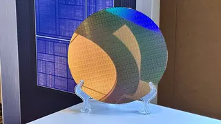 A photo of an Intel 18A wafer, full of Panther Lake compute tiles, with a stylized image of a complete PTL chip in the background.
