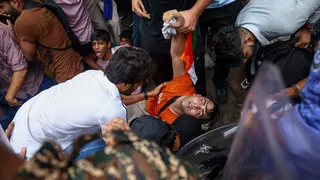 A man is held by the arms by onlookers, his eyes roll back in his head and he looks as if he is losing consciousness