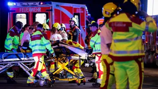 A number of emergency services personnel standing near an ambulance, with a person on a stretcher