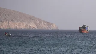 A large and small vessel are seen in the water, with land in the background