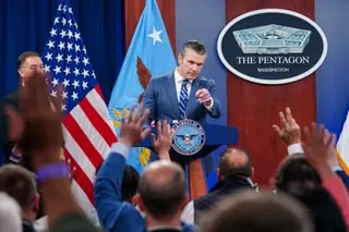 man in suit standing at lectern points finger toward people raising hands