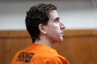 Bryan Kohberger in an orange prison uniform with curly hair looks upward in profile in a courtroom