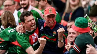 A crowd of people. In focus are two men with their arms around each others' shoulders. They are both wearing red and green sports tops.