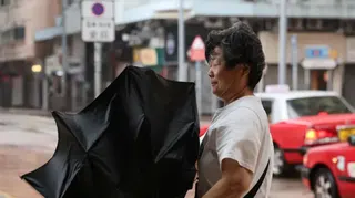 一名行人在香港受颱風「羅莎」（Noul）帶來的暴雨和強風影響下撐傘前行；強風吹得雨傘向上翻起