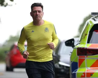 Andy Burnham jogging alongside a police car.