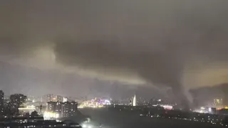 A giant tornado sweeping a city in the night, with the skyline of a city behind it