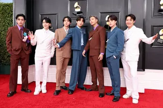 BTS stand in a line while posing wearing suits with the Grammys logo in the bacgkround, at the 2022 Grammys red carpet