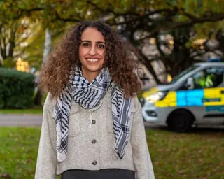 Huda Ammori smiles at the camera wearing a beige cardigan and patterned scarf