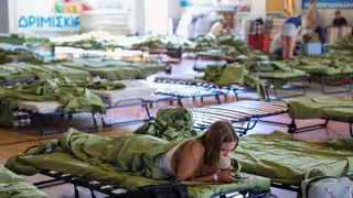 A tourist takes shelter at the sports hall of the town of Moires as a wildfire burns on the island of Crete,