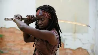Michonne (Danai Gurira), a Black woman with dreadlocks held back by a colorful bandana, stands in a ready stance with a katana in The Walking Dead