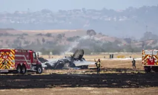 Fire crews spray water on the charred wreckage of an aircraft on an airfield
