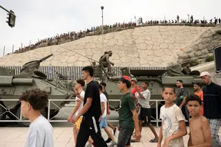 移民们周五大摇大摆走过摩洛哥和西班牙北非飞地休达之间的边境，经过西班牙军方人员和军车。（图取自法新社）
