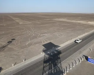 A Nazca Lines geoglyph carved into desert ground is visible beside a highway with a white truck