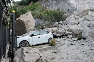 A car sits crushed under rocks outside a gate