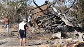 Jewish settlers, wearing religious garments, stand around the remains of a burnt building and car, in Havat Gilad (19/07/26)