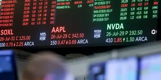 Trading monitors display SOXL, AAPL, and NVDA options quotes above a blurred workstation and person.
