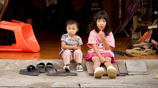 A young girl sitting on the roadside with another young child in Mae Sot, Thailand, on the border with Myanmar
