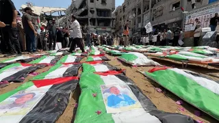 Palestinian flags and photographs are laid over bags containing the remains of 112 members of the Hassayna and Abu Sharia clans who the Civil Defence says were killed in an Israeli strike in November 2023, at a mass funeral in Gaza City, northern Gaza (4 August 2026)