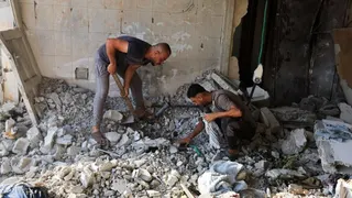 Two men search through rubble