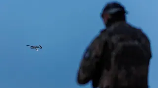 A Ukrainian soldier operating a drone, which is flying in the air in the background