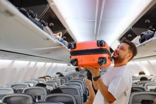 Man putting hand baggage in lockers above seats of plane