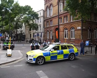 Police officers stand near a patrol car behind cordon tape on Endell Street, Covent Garden