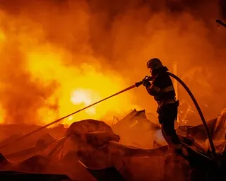 A firefighter silhouetted against flames sprays water at a fire in Kyiv