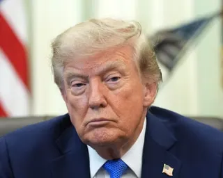 President Trump sits with a serious, downcast expression, flags blurred behind him in the Oval Office