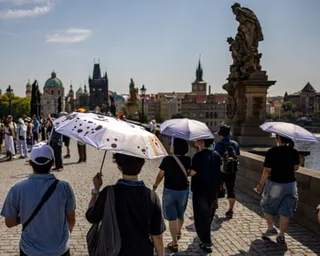 People walking across a bridge in Prague use umbrellas to shade themselves from the sun