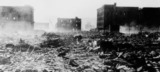 一张黑白照片展示了 1945 年日本广岛原子弹爆炸后的废墟与破坏景象，背景中的原子弹圆顶在断壁残垣中清晰可见。