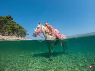 席卷欧洲的热浪逐渐往东转移，克罗地亚著名旅游景点布拉奇岛上，一名女游人骑着马泡在海水中。 （路透社）