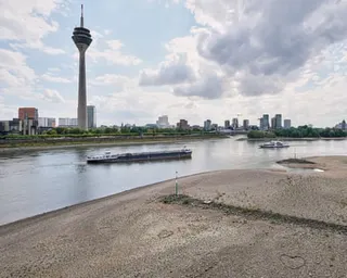 A barge travels the Rhine past Düsseldorf's skyline, with sandy banks exposed by low water levels