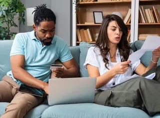 Stock image of a couple on a sofa looking at a laptop and a paper bill