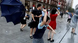 白海豚颱風來臨前風勢增強之際，上海街頭有民眾撐傘行走，其中一名男童正試圖抓緊一把被吹翻的雨傘（9/8/2026）