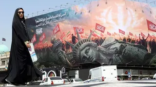 A veiled Iranian woman walks past an anti-US billboard at Enghelab Square in central Tehran